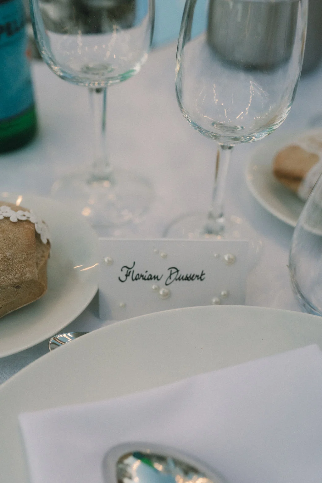 Détail d'une table de mariage blanche avec un marque-place calligraphié au nom de Florian et des verres à pied.