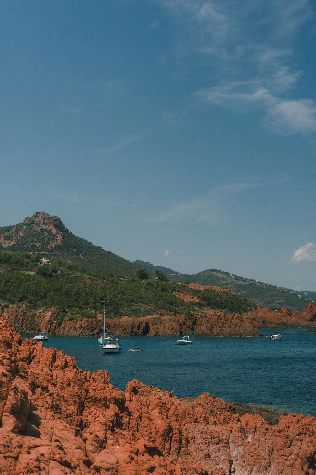 Vue panoramique sur les roches rouges et les eaux turquoise du Cap Roux avec quelques bateaux à l'ancre.
