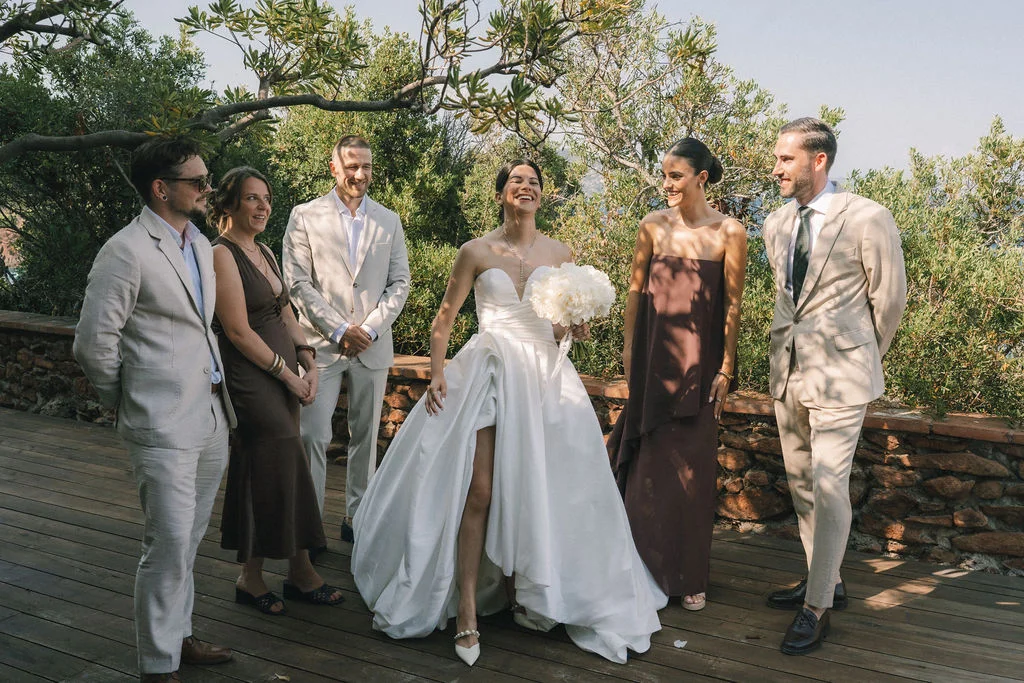 Une mariée en robe blanche et ses invités élégants posent en extérieur dans un cadre naturel et lumineux.