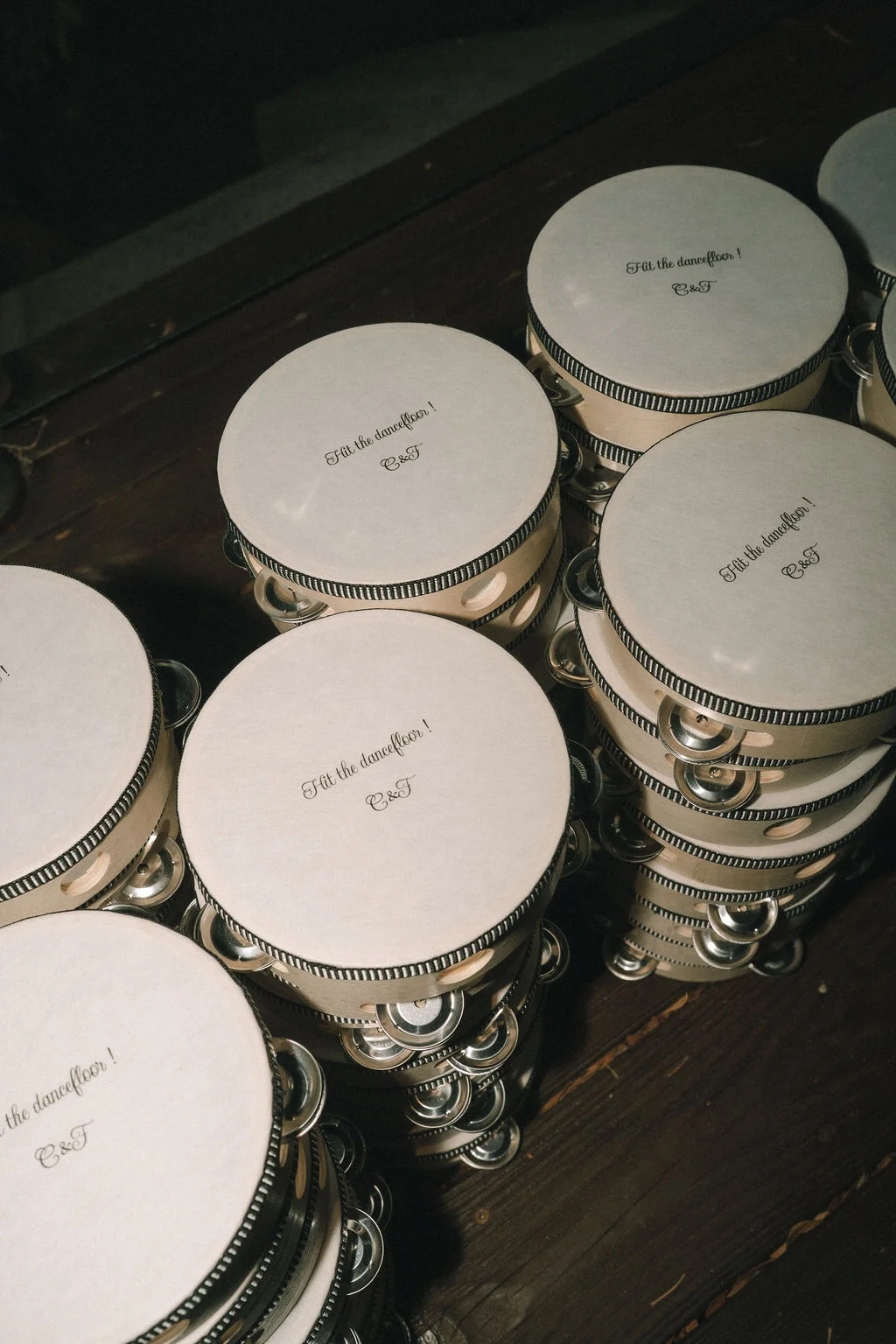 Tambourins blancs personnalisés C&T alignés sur une table en bois sombre pour l'animation d'un mariage.