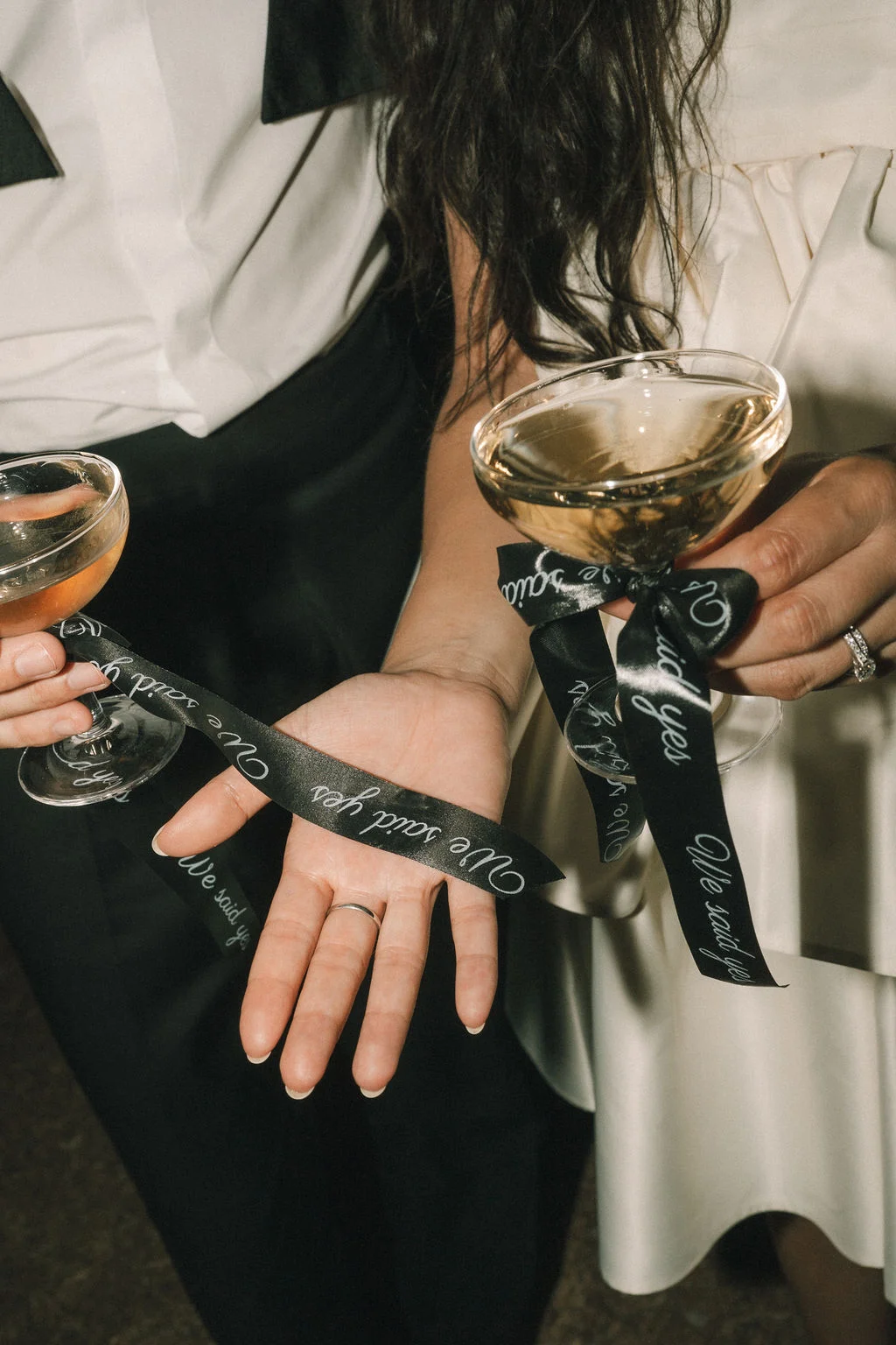 Gros plan stylé d'un couple tenant des coupes de champagne, liés par un ruban noir marqué We said yes.