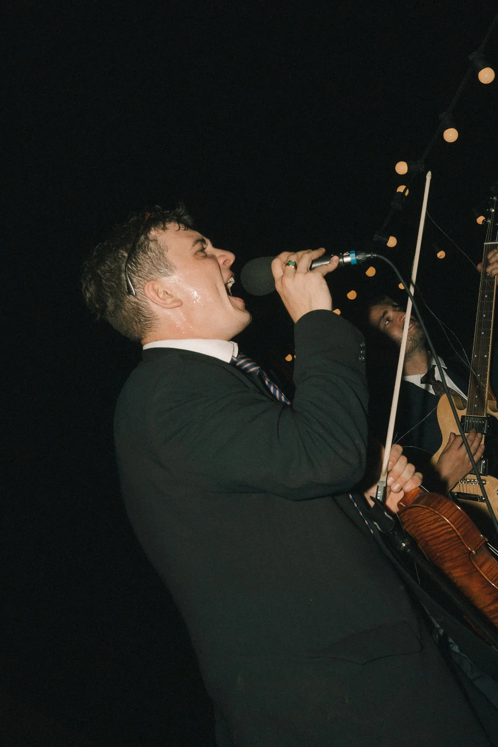 Un homme en costume noir chante avec passion dans un micro lors d'une soirée festive nocturne.