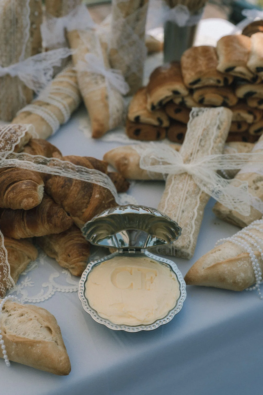 Buffet de pains artisanaux et croissants avec un beurre monogrammé, décoré de dentelle blanche sur un nappage bleu clair.