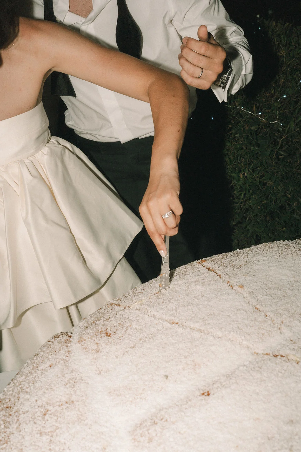 Un couple élégant découpe ensemble un grand gâteau blanc saupoudré de sucre glace lors de leur réception de mariage.