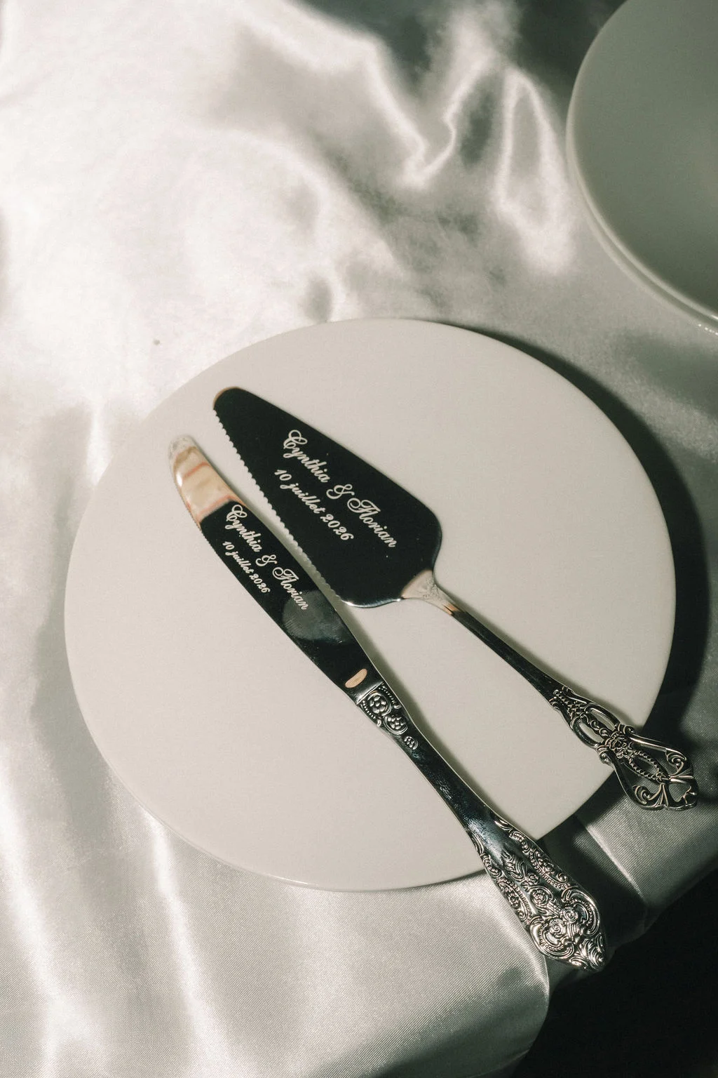 Couteau et pelle à gâteau personnalisés posés sur une assiette blanche et un nappage satiné argenté.