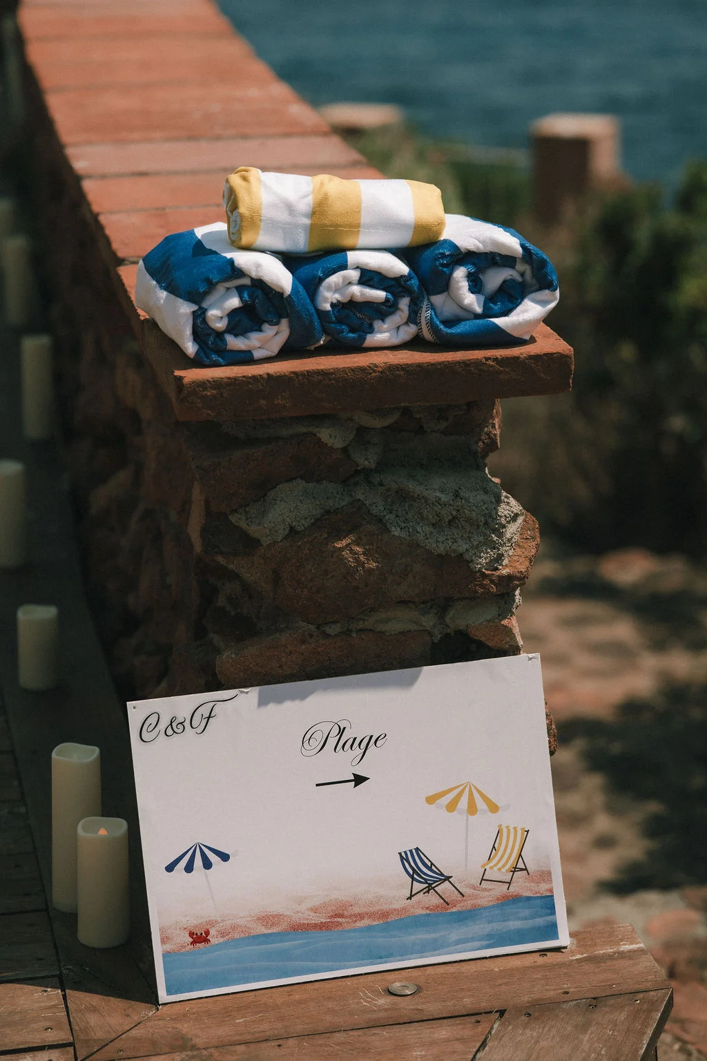Serviettes de plage bleues et jaunes et panneau directionnel pour le mariage de C&F sur un muret en pierre.