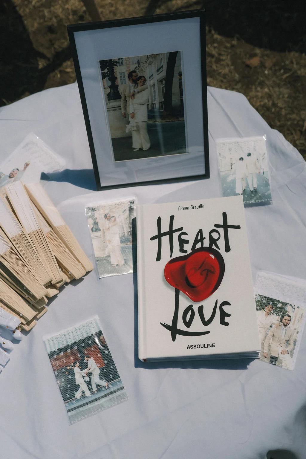Livre d'art Heart Love, photos de couple et livrets sur une nappe blanche pour un mariage élégant et stylé.