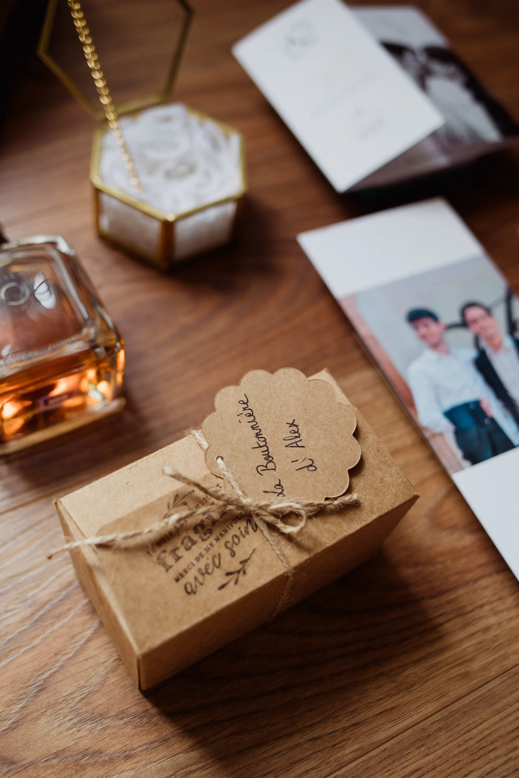 Petit cadeau emballé de papier kraft avec une étiquette manuscrite, entouré d'accessoires de mariage sur un bois chaleureux.