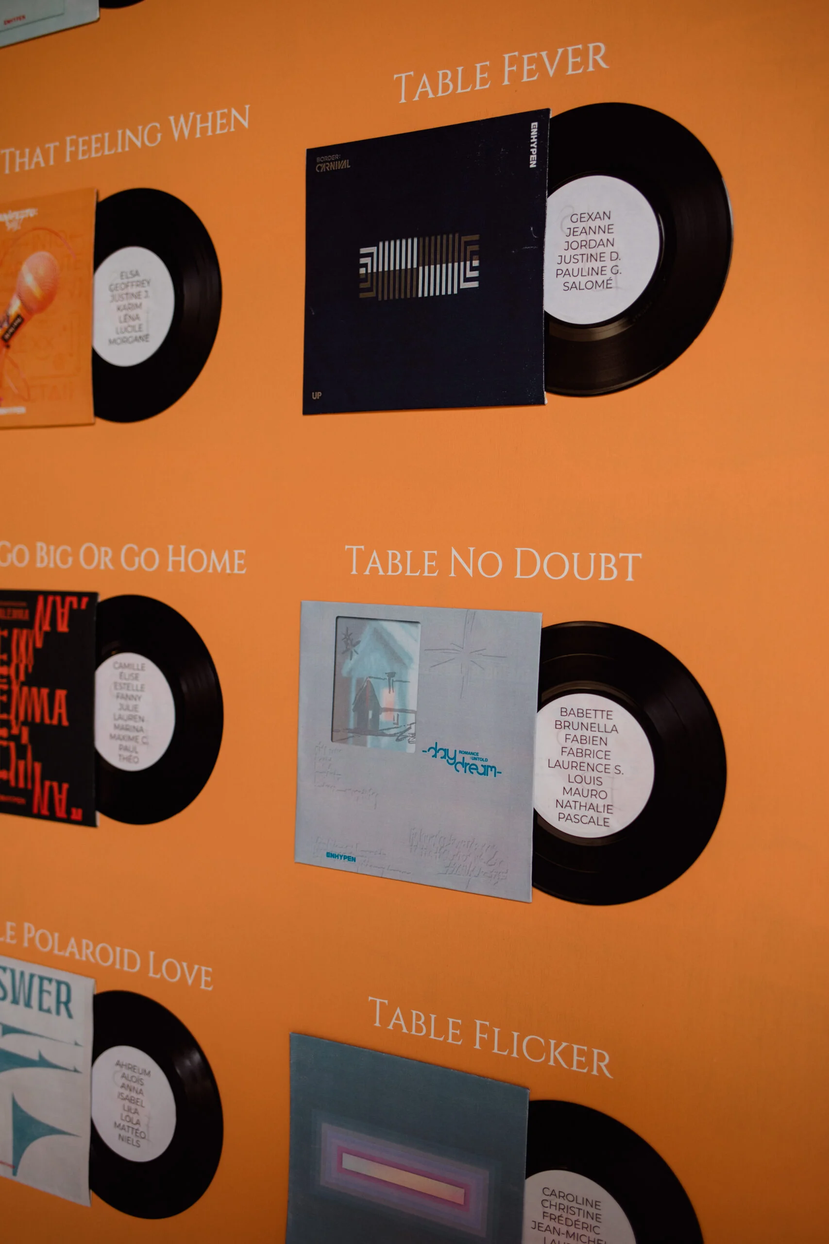 Disques vinyles et pochettes colorées exposés sur un mur orange avec des inscriptions poétiques en blanc.