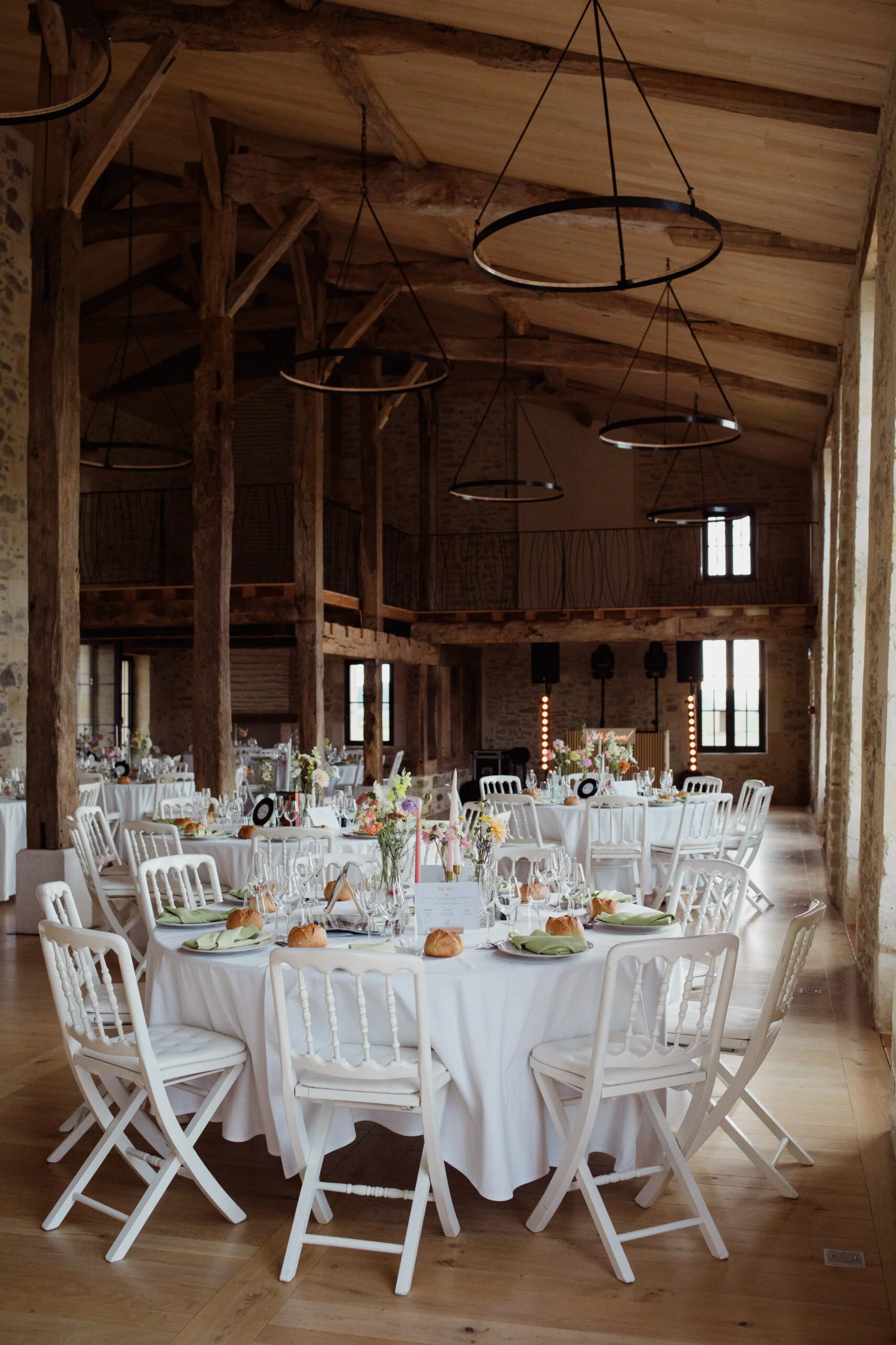 Réception de mariage dans une grange rustique avec tables rondes nappées de blanc et décorations florales pastel.
