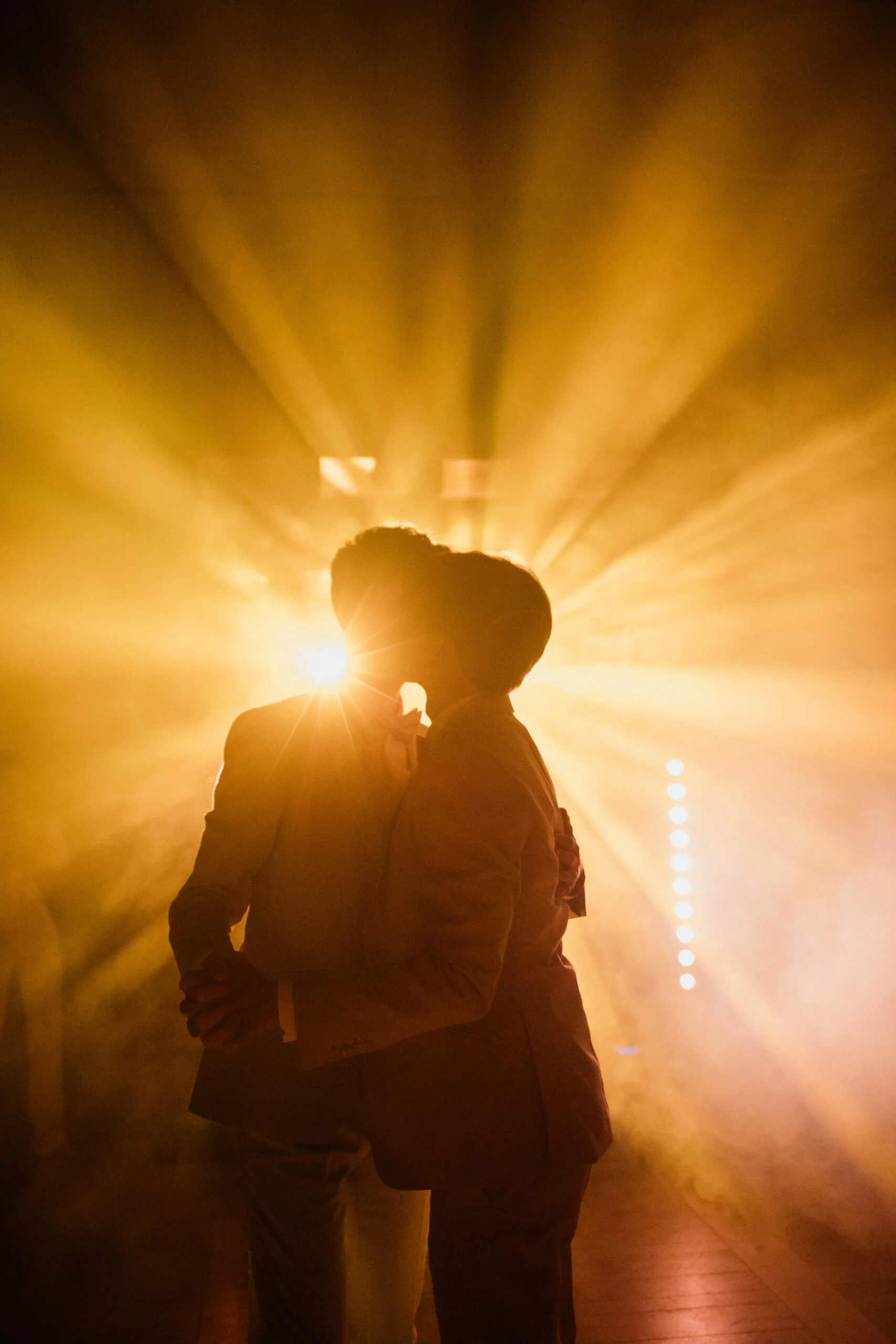 Silhouette d'un couple d'hommes s'embrassant dans une ambiance onirique et brumeuse aux tons dorés et lumineux.