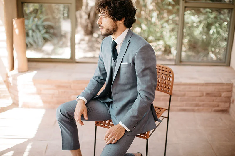 Un homme élégant dans un costume bleu marine et un chaise en bambou, incarnant la sophistication et l'originalité pour