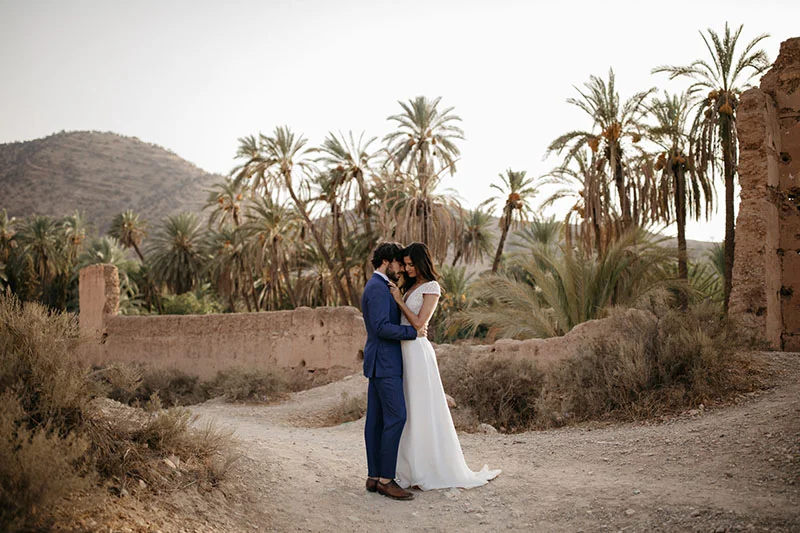 Un couple romantique dans des costumes élégants, se tenant dans un décor pittoresque avec des palmiers et des ruines,
