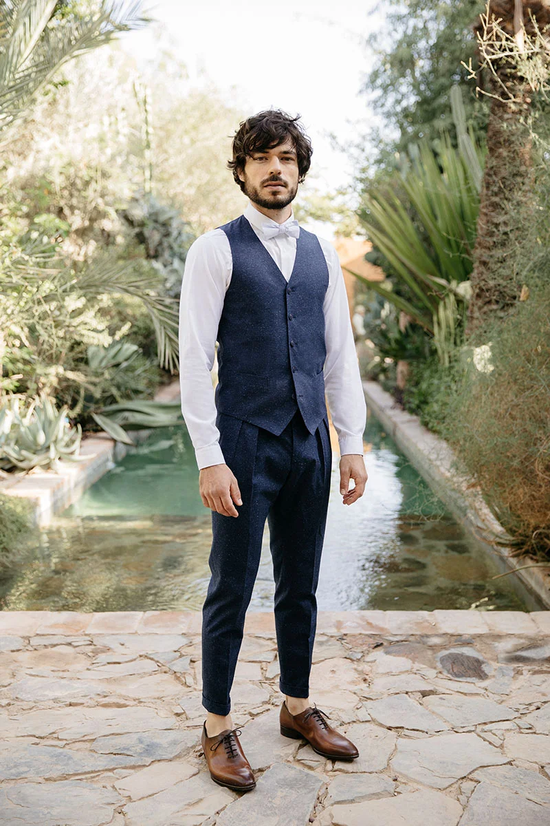 Elegance et audace : un homme habillé d'un veston marine et de pantalon sombre, orné d'un cravate blanche et d'un