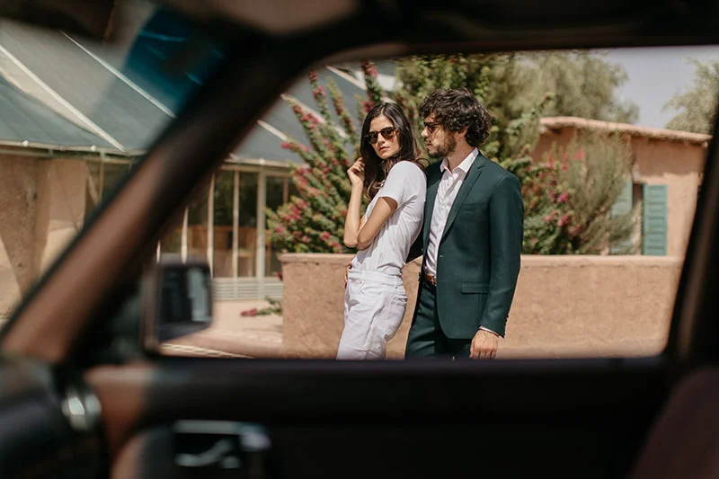Un couple élégant dans des vêtements blancs et verts, capturé à travers la fenêtre d'un véhicule, incarnant l'élégance
