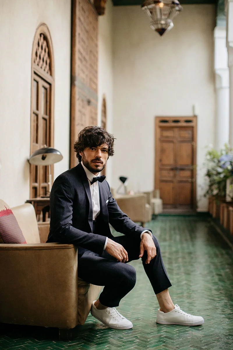 Élegance et audace se rejoignent dans un look de mariage unique, avec un smoking noir et des chaussures blanches modernes.