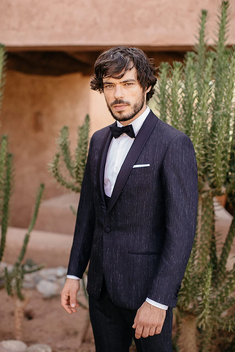 Élegance raffinée et audace de style : un homme habillé d'un costume noir brillant avec des accents blancs, se détache