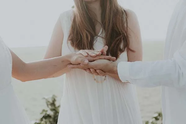 Une scène tendre de mariage en bord de mer avec des mariés vêtus de blanc et des mains tendues, symbolisant l'union.