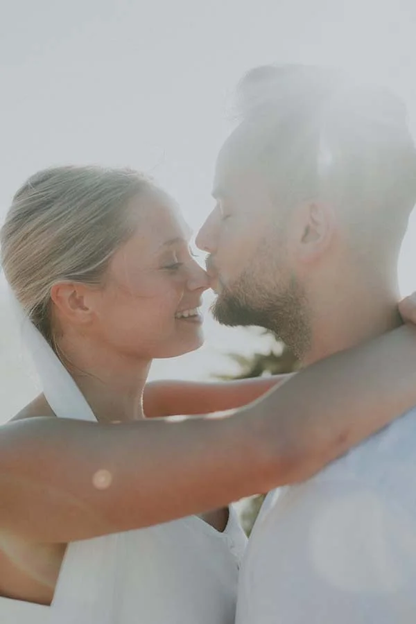Un couple heureux dans des vêtements blancs, échangeant un baiser tendre sur une plage paisible au Pays de Loire.