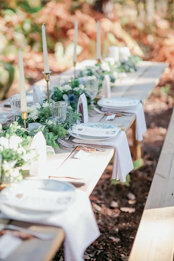 Table de mariage champêtre en bois avec décoration florale blanche et bougies, dans un cadre naturel et lumineux.