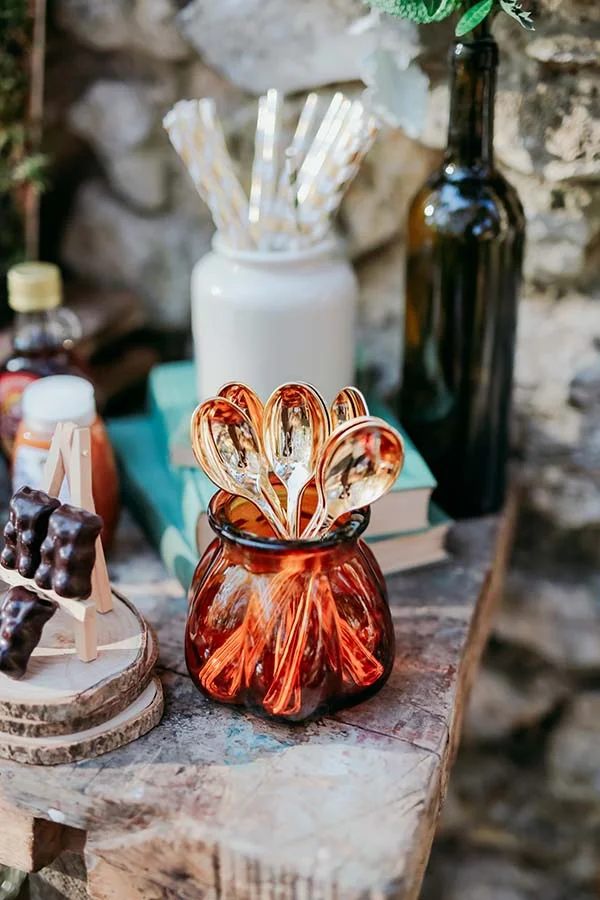 Cuillères dorées dans un vase ambré sur une table rustique, ambiance champêtre et chaleureuse.