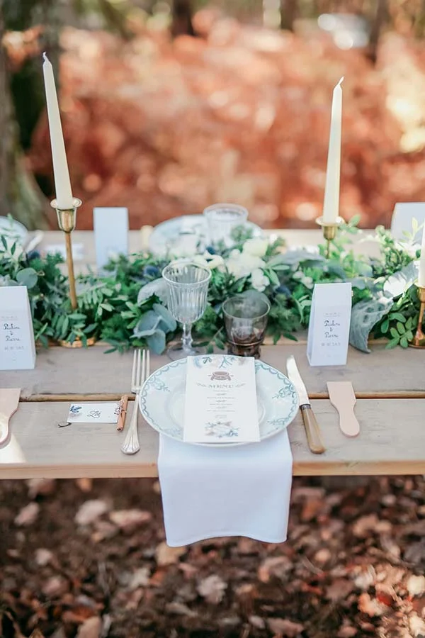 Table de mariage champêtre avec décoration végétale, bougies blanches et vaisselle raffinée dans un sous-bois automnal.