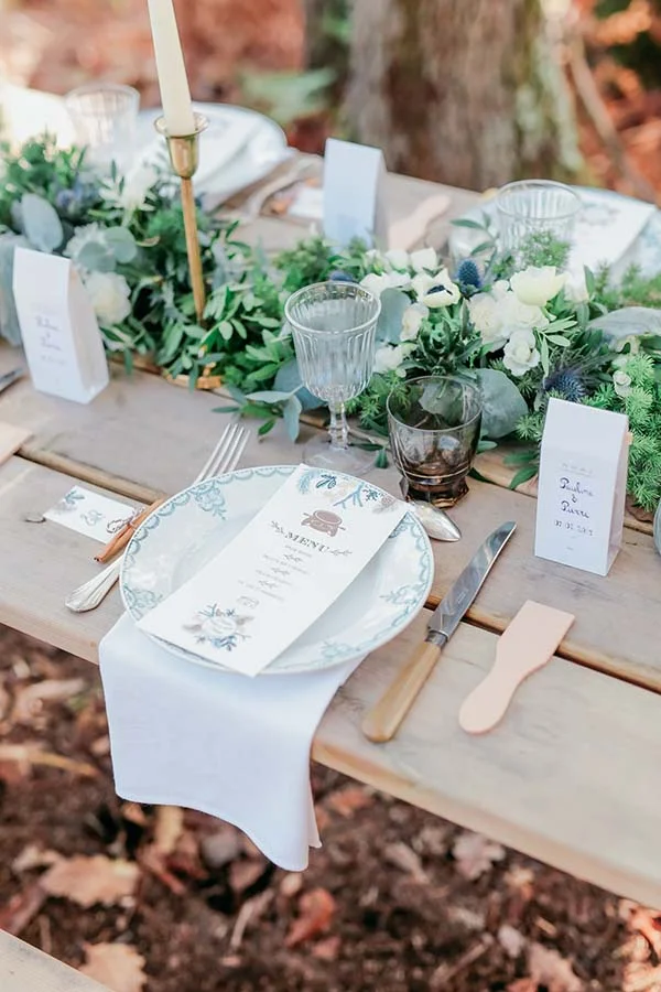 Table champêtre élégante avec vaisselle blanche, menu personnalisé et décoration végétale blanche et verte.