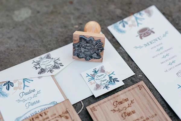 Papeterie de mariage champêtre avec tampons personnalisés, menus et noms d'invités sur papier blanc et bois clair.