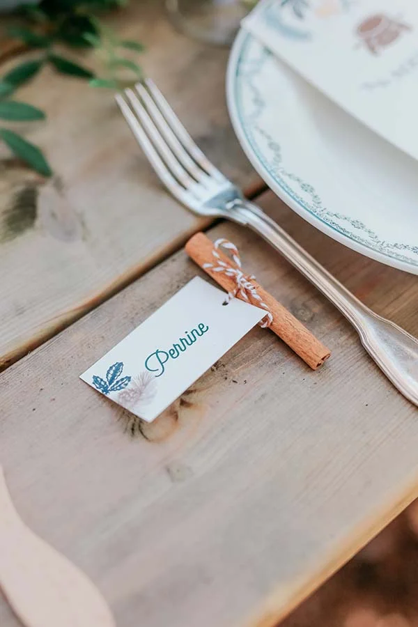 Marque-place personnalisé attaché à un bâton de cannelle sur une table en bois rustique pour un mariage champêtre.