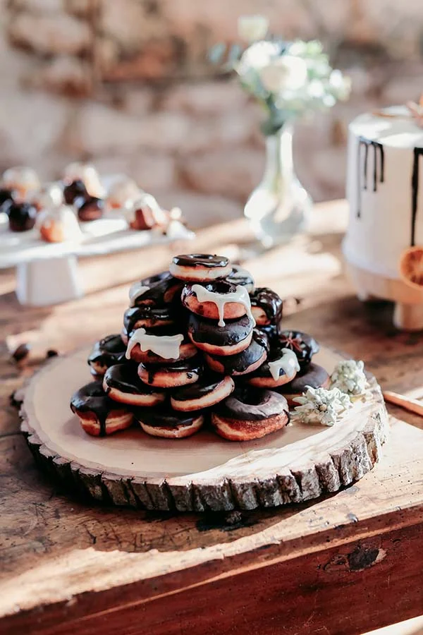 Pyramide de donuts au chocolat et glaçage blanc sur un plateau en bois brut, ambiance champêtre et chaleureuse.