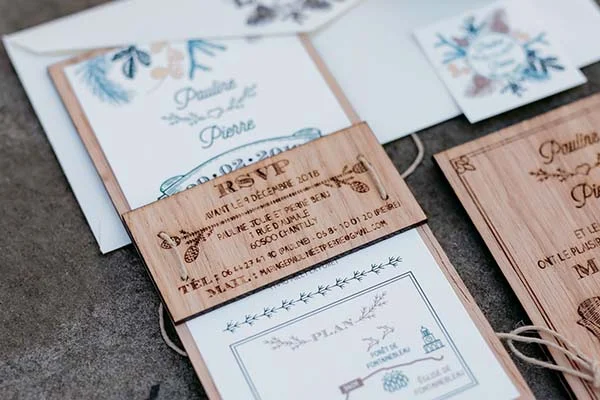 Faire-part de mariage champêtre sur papier blanc et bois clair avec des illustrations botaniques bleues.