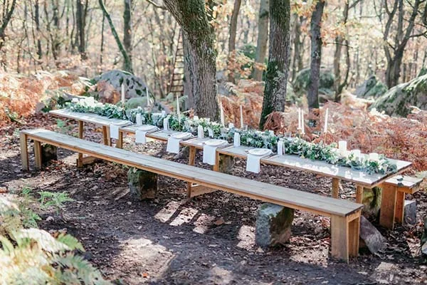 Longue table en bois décorée de feuillage et bougies blanches pour un banquet champêtre en pleine forêt.