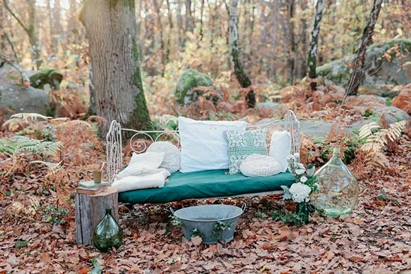 Espace lounge champêtre avec banquette vert émeraude et coussins blancs installée dans une forêt aux tons automnaux.