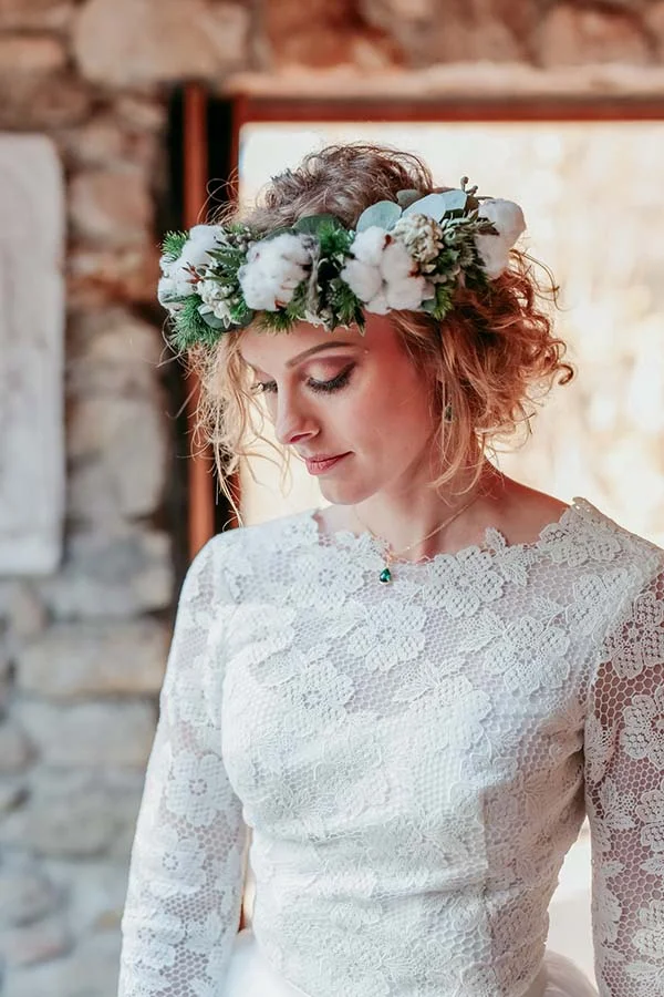 Mariée en robe de dentelle blanche portant une couronne de fleurs champêtres, dans un cadre rustique et lumineux.
