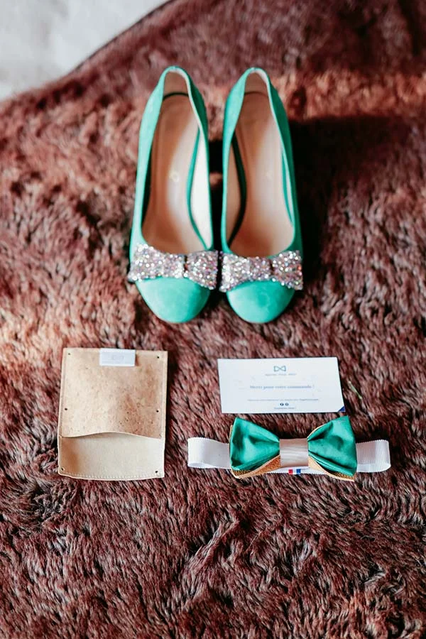 Chaussures à talons vertes à strass, nœud papillon assorti et accessoires posés sur un tapis en fourrure brune.