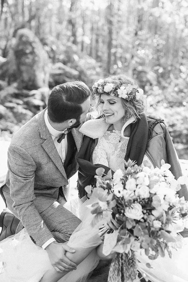 Couple marié en noir et blanc dans un cadre naturel, la mariée portant une couronne de fleurs et un bouquet champêtre.