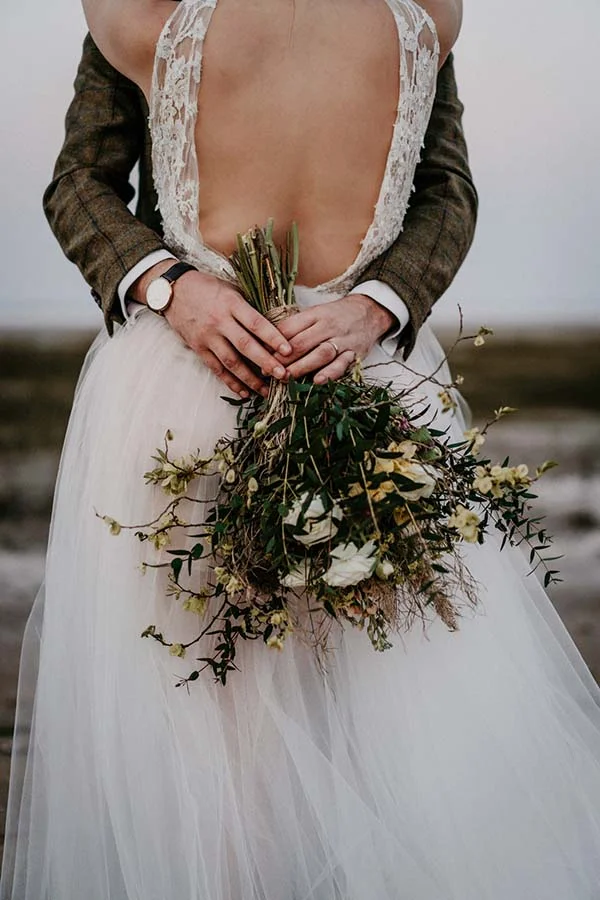 Un couple en mariée et mari, tenant un bouquet naturel et romantique, incarnant l'ambiance d'un mariage écologique et sauvage.
