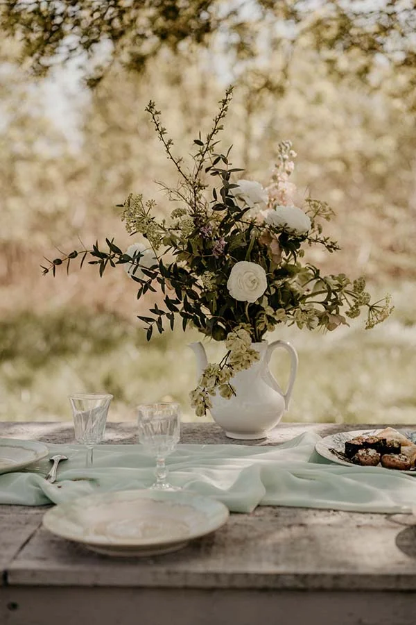 Tableau idyllique d'un mariage naturel et éco-responsable, avec un bouquet de fleurs blanches et vertes dans un bol