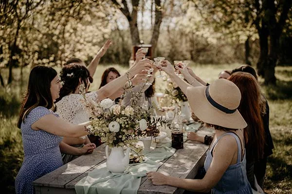 Groupe de femmes célébrant autour d'une table avec fleurs et verres, dans un parc charmant et éco-responsable.