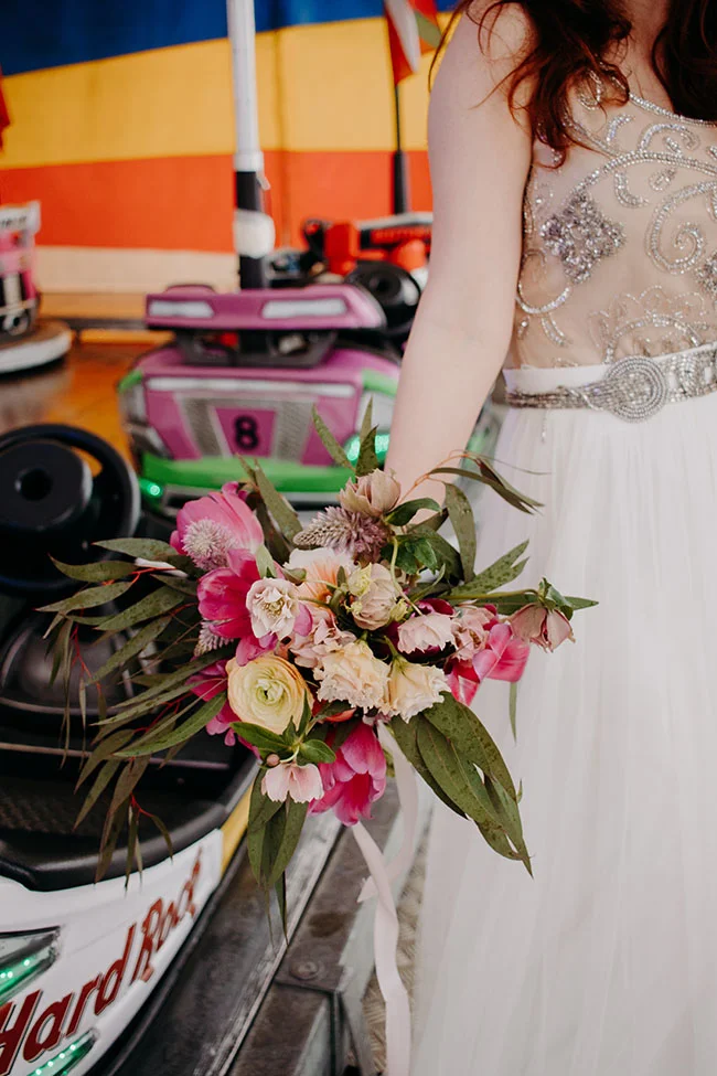 Une jeune femme en robe blanche et vêtement orné tient un bouquet de fleurs colorées, avec un arrière-plan de bulles de