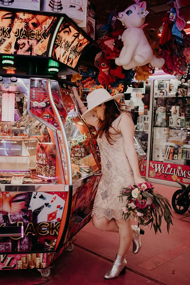 Une jeune femme dans un hat blanc et des bottes argentées se tient devant un machine à sous au thème du blackjack,