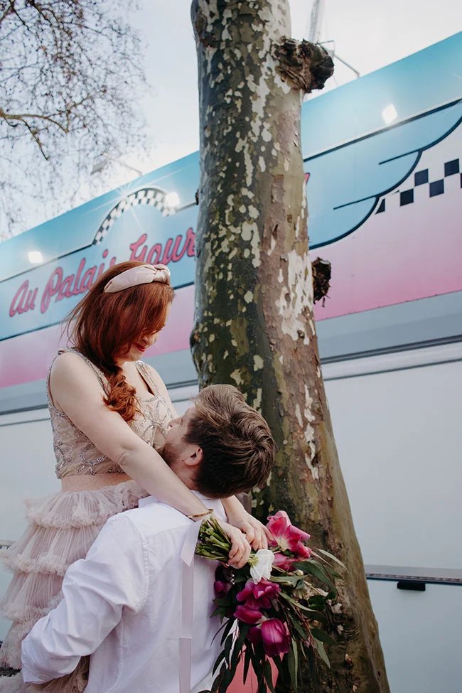 Un couple romantique contre un décor coloré, avec une femme tenant une bouquet de fleurs, pour un shooting romantique à