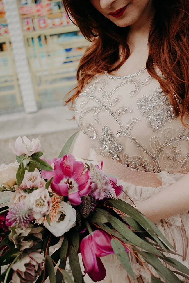 Élégante mariée tenant un bouquet coloré, habillée dans un robe orné de perles, dans un décor vibrante et joyeux.