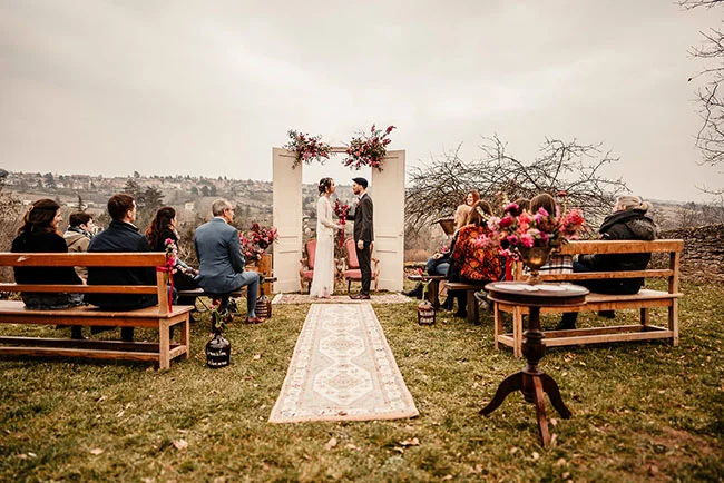 Un mariage vintage et magenta avec un décor charmeux en plein air, un arche fleuri et une couverture de tapis raffinée.
