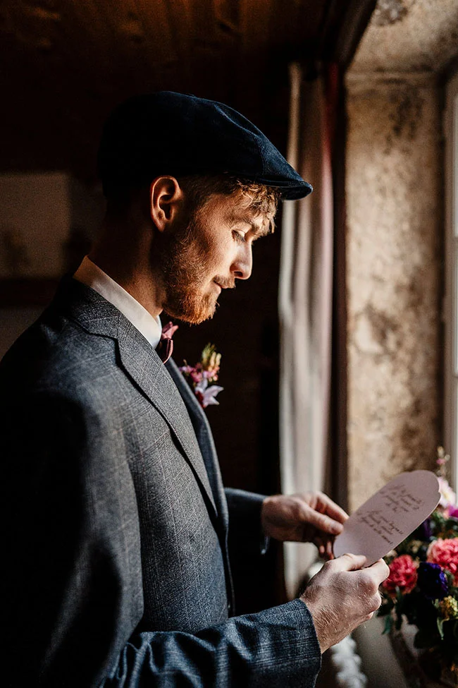 Un homme élégant examine un programme de mariage vintage, avec un fond de fleurs magenta.