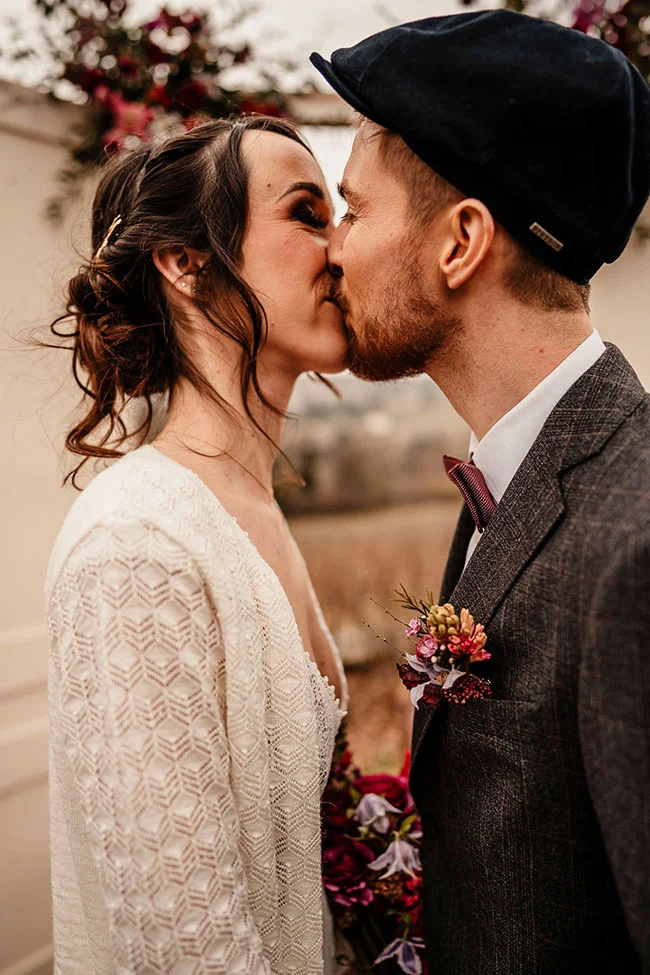 Un couple romantique partage un baiser tendre, entouré de détails de mariage vintage et de tons magenta.