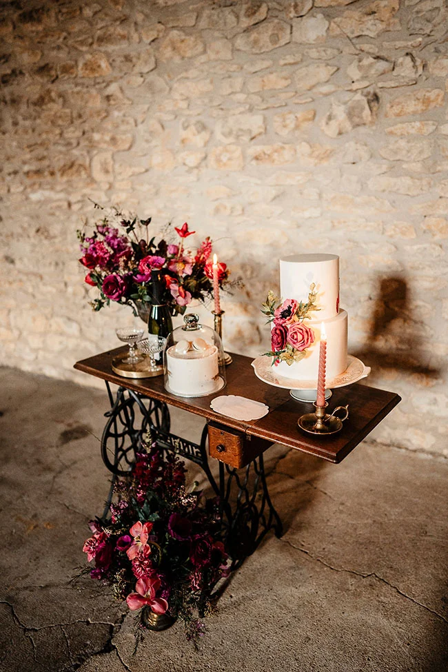 Un mariage vintage et magenta avec un gâteau à deux étages orné de fleurs rouges et roses, accompagné d'une décoration