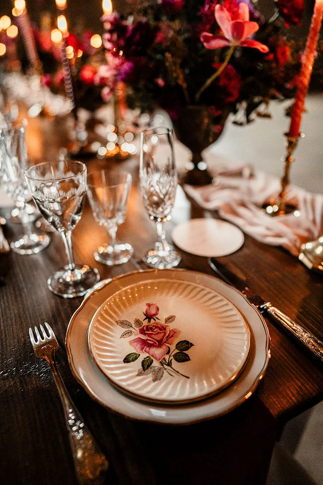 Tableau de banquet romantique avec un plateau fleuri et verres à vin, illuminé par des cierges et des fleurs magenta,
