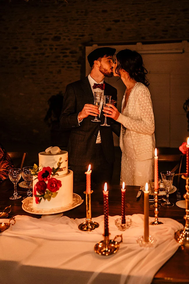 Un couple charmant partageant un baiser romantique autour d'un gâteau en deux étages décoré de roses rouges, entouré