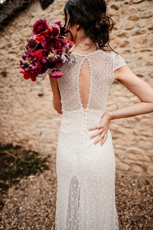 Une mariée en robe blanche délicieuse tient un bouquet de fleurs magenta en plein air, créant un contraste saisissant.